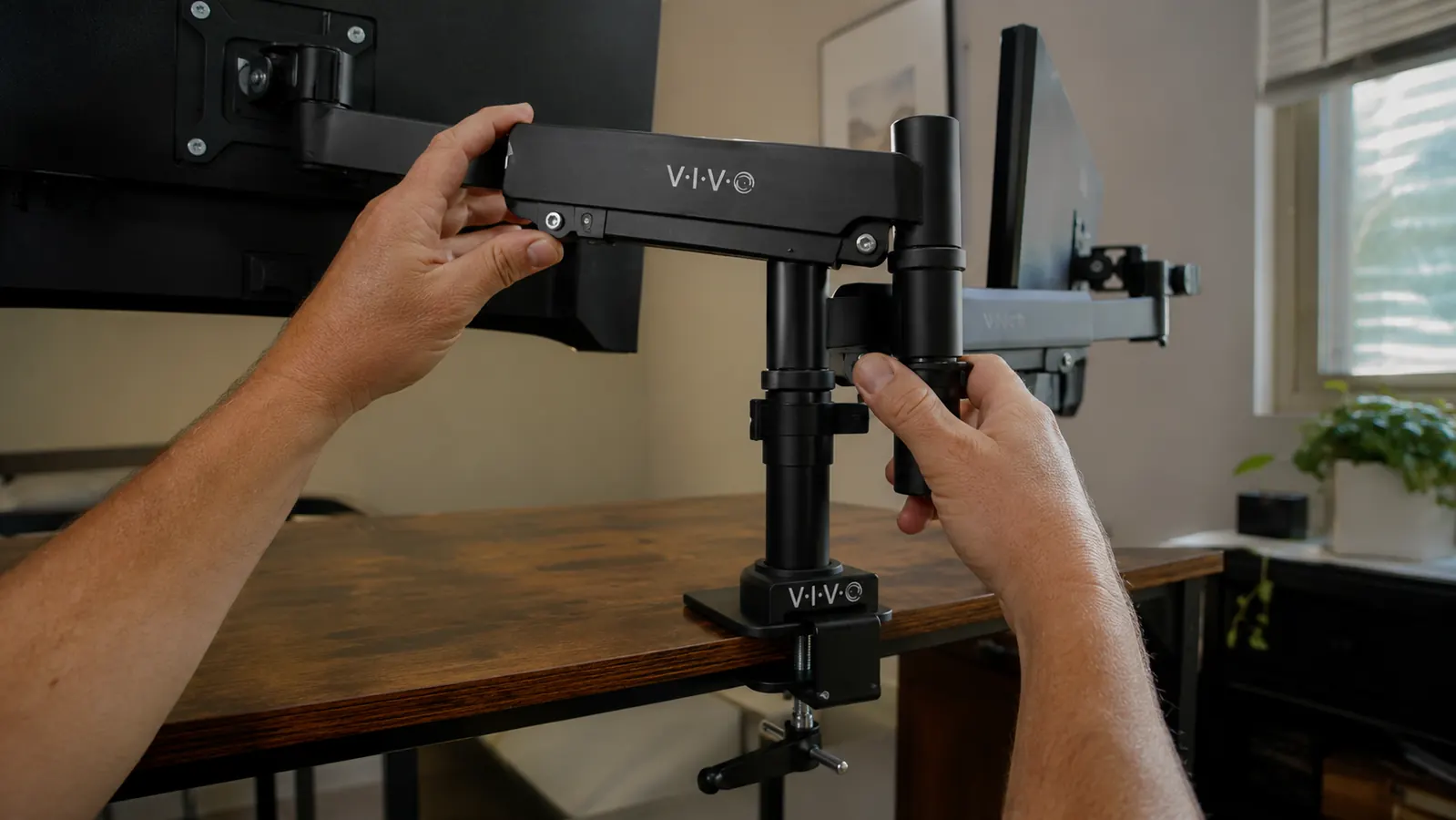 Hand adjusting the VIVO dual monitor desk mount arm to change screen height