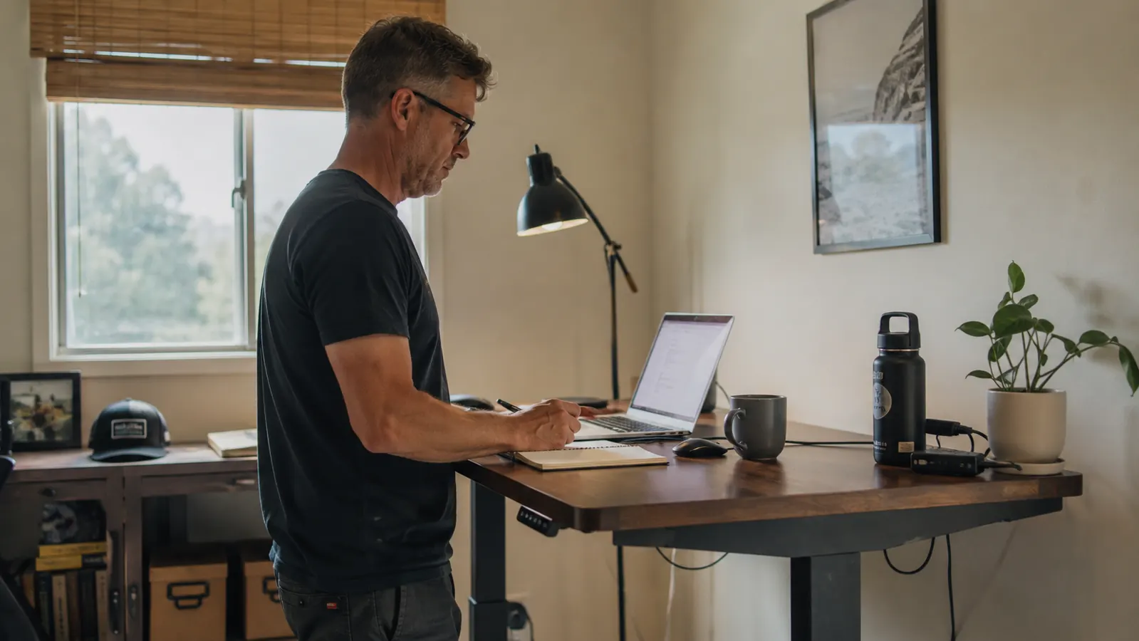 Man standing at a raised home office desk working on a laptop in a small spare bedroom