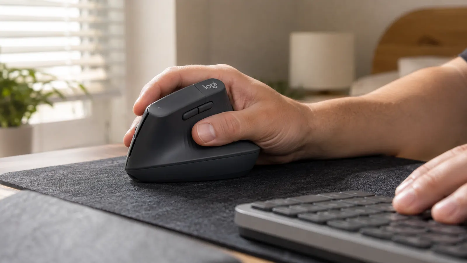 Hand gripping the Logitech Lift vertical mouse in a relaxed handshake position on a desk mat
