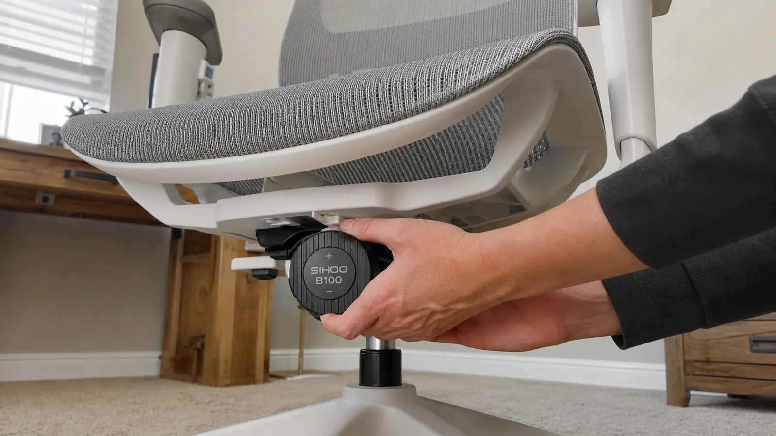 Hand reaching underneath the SIHOO B100 seat to adjust the tilt tension knob