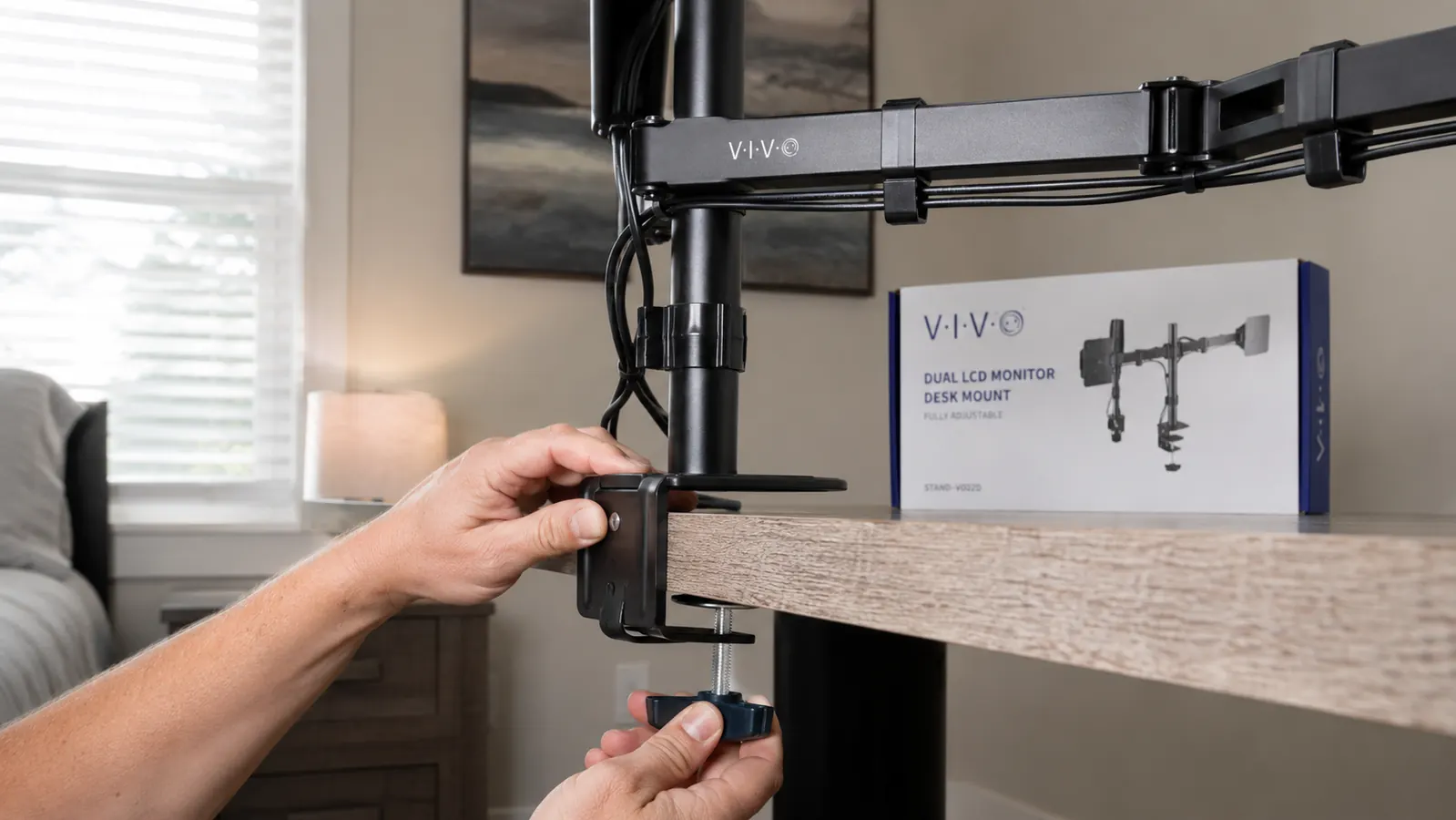 Close-up of a hand clamping the VIVO monitor mount to the back edge of a wood desk