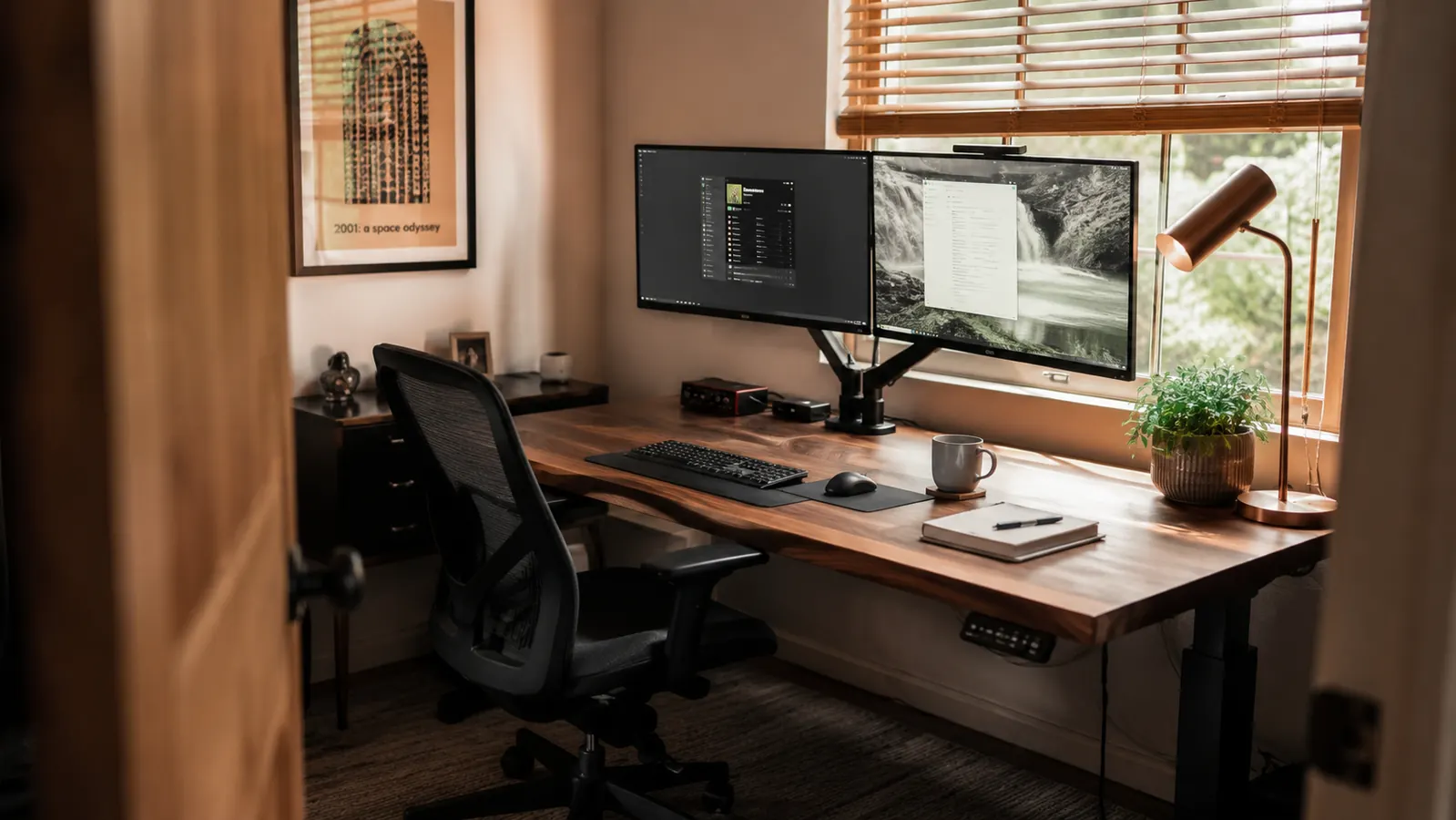 Small home office spare bedroom desk with dual monitors raised on an arm mount at eye level, warm morning light