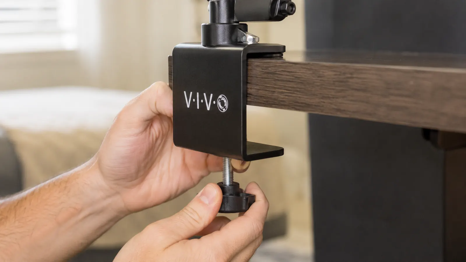 Hand tightening the C-clamp of the VIVO dual monitor mount onto the back edge of a desk